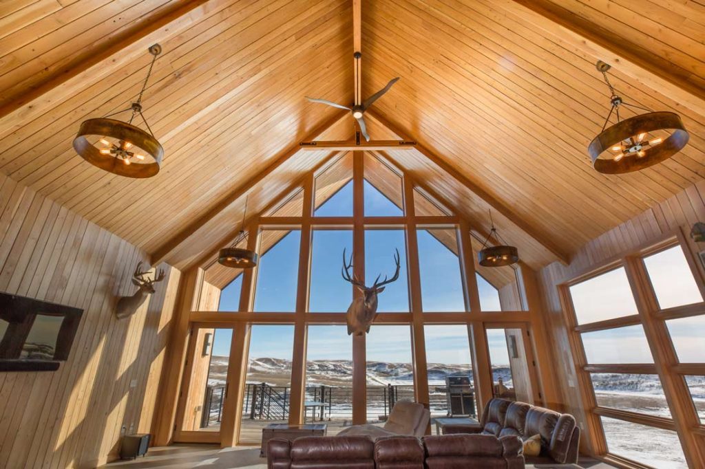 Interior of a living room featuring many windows looking out to the open prairie land and floor to ceiling woodwork