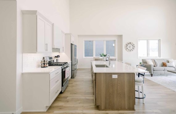 Interior of an open concept kitchen area that features neutral colors and vinyl flooring